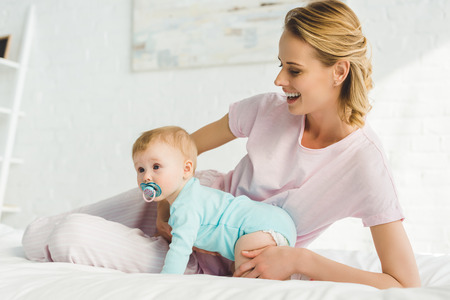 Smiling mother holding infant daughter with baby dummy