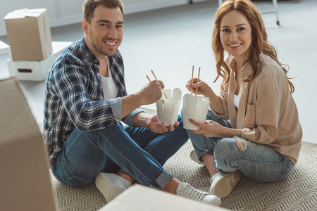smiling couple eating asian food at new apartment, moving home conceptの写真素材