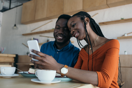 cheerful african american couple using smartphone together in coffee shopの写真素材