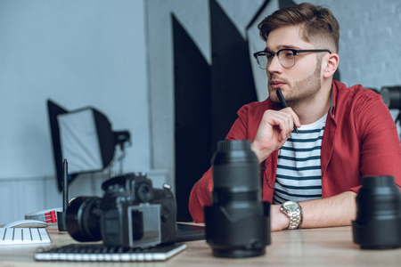 Thoughtful freelancer working by table with cameraの写真素材