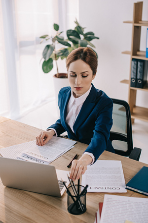 focused businesswoman in suit doing paperwork at workplace in officeの写真素材