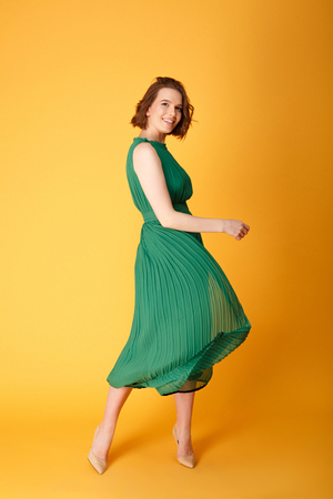 young beautiful woman in green dress dancing isolated on orangeの写真素材