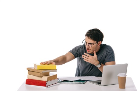 shocked handsome student looking at stack of books isolated on white