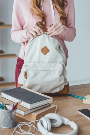 cropped view of female student with backpack, headphones and books on tableの写真素材
