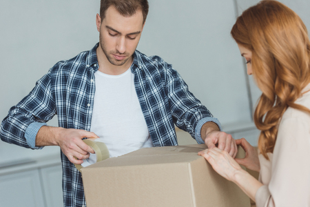 couple packing cardboard box with sticky tape together, relocation conceptの写真素材