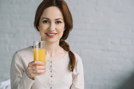 beautiful woman holding glass of orange juice and looking at cameraの写真素材