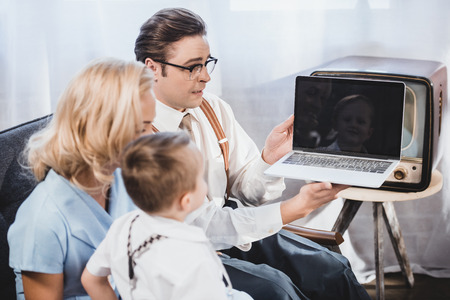 1950s family with one child holding laptop with blank screen at homeの写真素材
