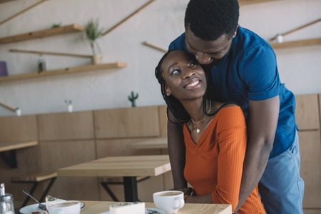 african american man hugging girlfriend on romantic date in coffee shopの写真素材