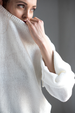 sensual young woman taking off white sweater and looking away on greyの写真素材