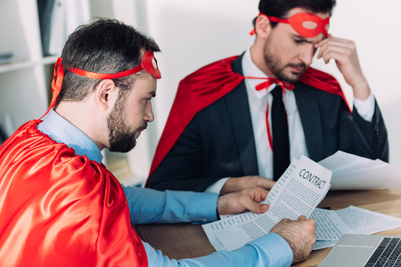 handsome super businessmen in masks and capes working with papers in officeの写真素材