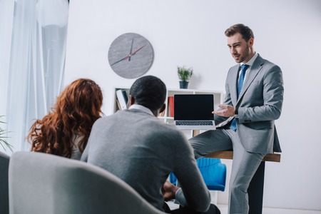 Financial adviser showing presentation on laptop to business colleaguesの写真素材