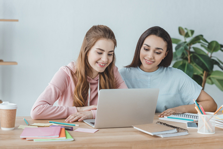 attractive multiethnic students using laptop at table with booksの写真素材