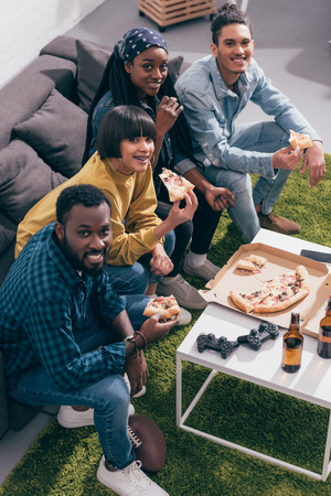 high angle view of young multiethnic friends sitting with pizza sitting on couchの写真素材
