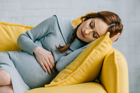 beautiful pregnant woman sleeping on yellow sofa in living roomの写真素材