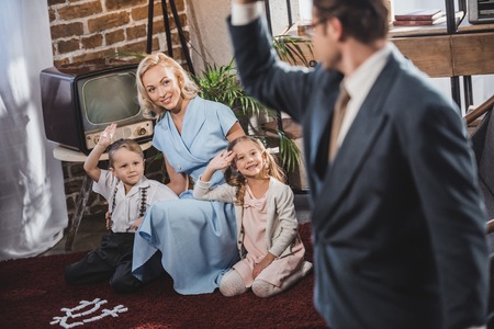 selective focus of father going to work and waving hand to happy family, 1950s style