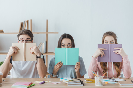 three young students holding books while sitting at tableの写真素材