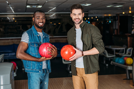 happy young men with balls at bowling club looking at cameraの写真素材