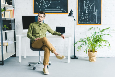 Stylish man sitting by table with computers at home officeの写真素材