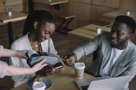 african american man paying for order with credit card while spending time with friend in cafeの写真素材