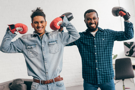 two smiling young men in boxing gloves standing with arms raisedの写真素材
