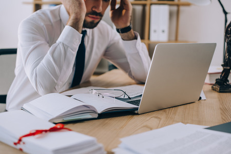 cropped shot of tired lawyer at workplace with documents and laptop in officeの写真素材