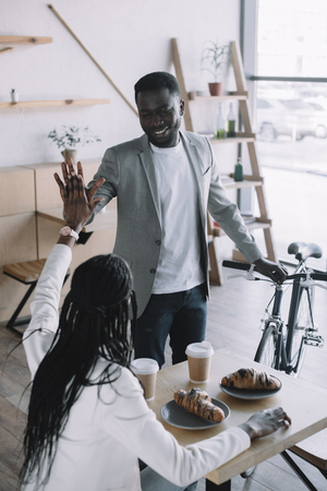 african american friends giving high five to each other at table in cafeの写真素材