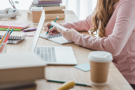 cropped view of female student studying with digital devices and books