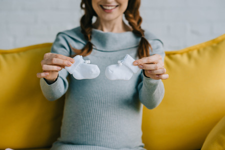 cropped image of pregnant woman showing newborn shoes in living roomの写真素材