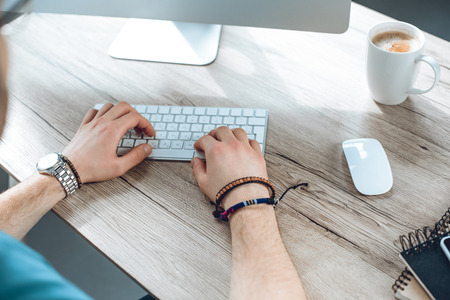cropped shot of man typing on keyboard and working with desktop computerの写真素材