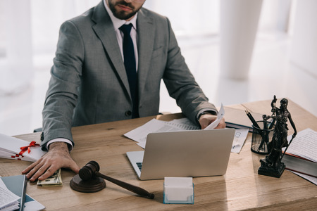 cropped shot of lawyer taking bribe at workplace with papers and laptop in office