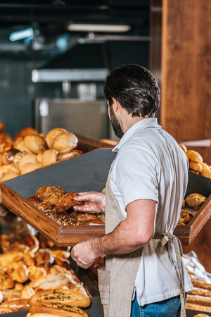 back view of male shop assistant arranging fresh bread in supermarketの写真素材