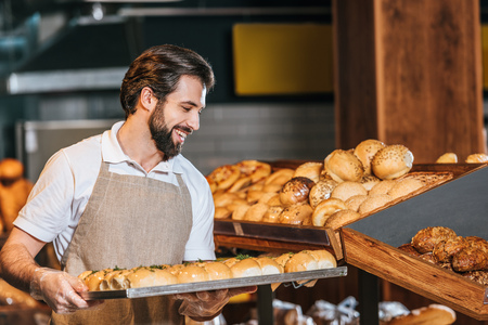 smiling male shop assistant arranging fresh pastry in supermarket