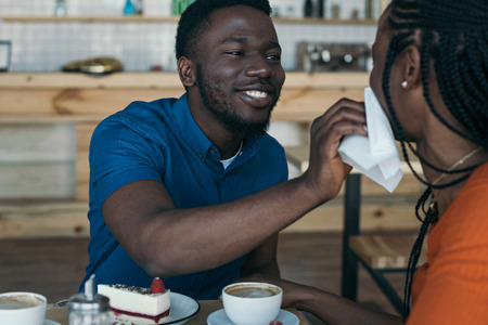 careful african american man cleaning girlfriends face with napkin at table in cafeの写真素材