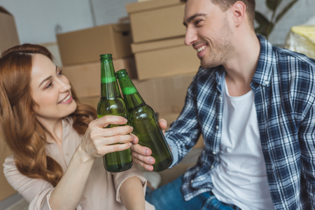 young couple clinking bottles of beer at new apartment, relocation conceptの写真素材