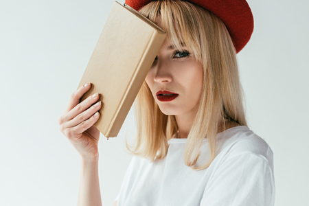 Fashionable blonde girl with red lips holding book isolated on greyの写真素材