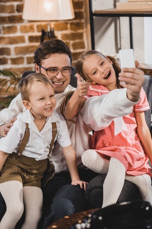 happy 1950s style family taking selfie with smartphone at homeの写真素材