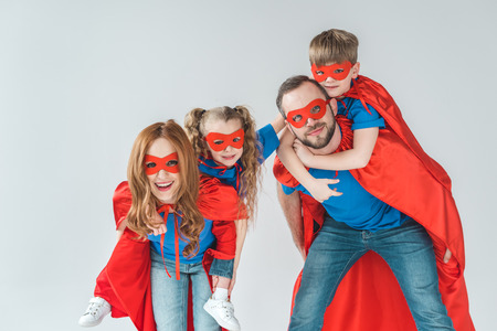 super parents piggybacking kids pretending to be superheroes isolated on greyの写真素材