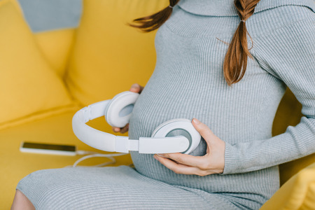 cropped image of pregnant woman putting headphones with music on belly in living room