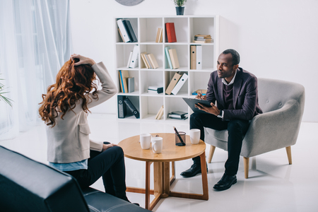 African american psychiatrist sitting in armchair and talking to female patientの写真素材