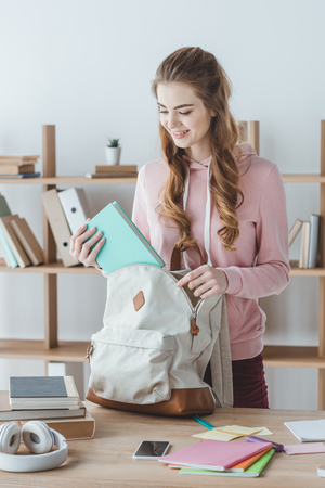 attractive smiling girl putting book into backpackの写真素材