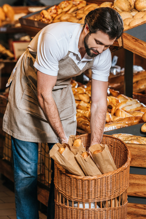 male shop assistant arranging fresh pastry in supermarketの写真素材
