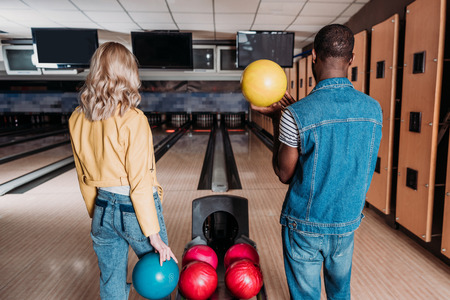 multiethnic couple with bowling balls standing in front of alleys at clubの写真素材
