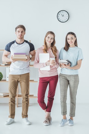 young students holding books, laptop, coffee and copybooks