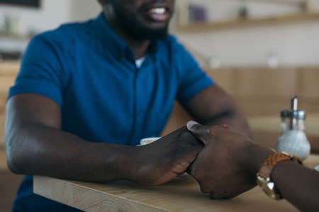 cropped shot of african american couple holding hands while sitting at table in cafeの写真素材
