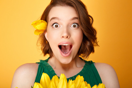 portrait of surprised woman with bouquet of yellow tulips isolated on orangeの写真素材