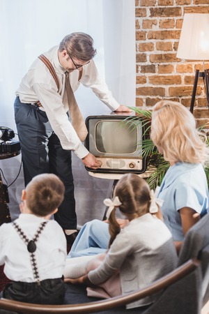 mother with two kids looking at father turning on vintage tv, 1950s styleの写真素材