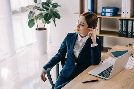 pensive businesswoman at workplace with documents and laptop in officeの写真素材