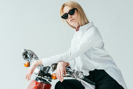 Attractive young woman in sunglasses on vintage scooter isolated on grey