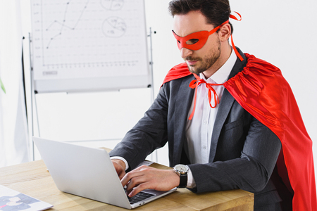 super businessman in mask and cape working with laptop in officeの写真素材