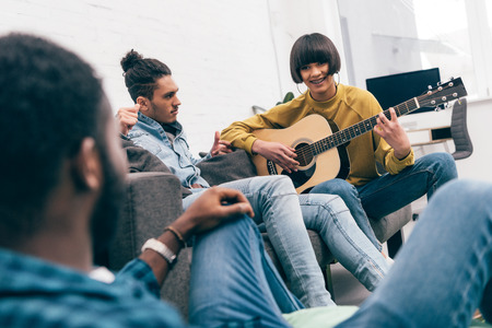 mixed race young woman playing on guitar to friendsの写真素材